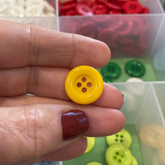 Hand holding a yellow button with a colorful button organizer in the background