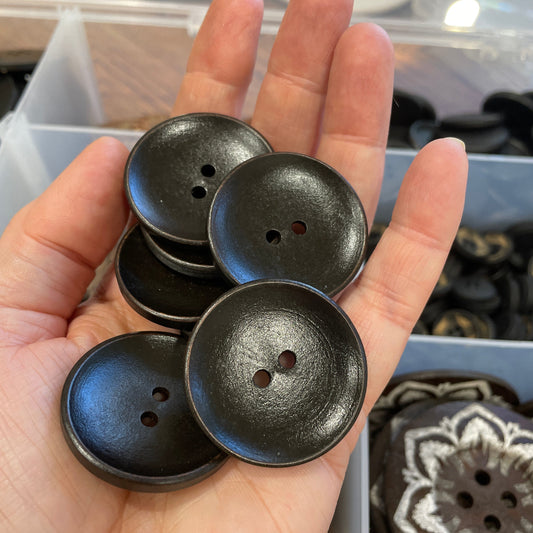 Hand holding black buttons with a blurred background of more buttons and fabric.