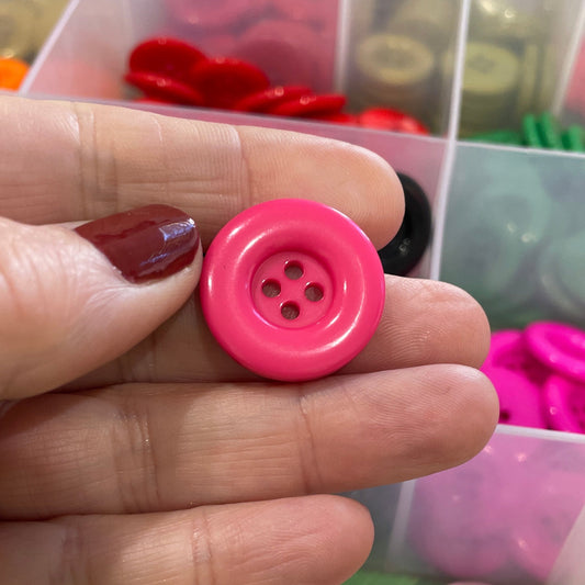 Hand holding a pink button with a container of colorful buttons in the background