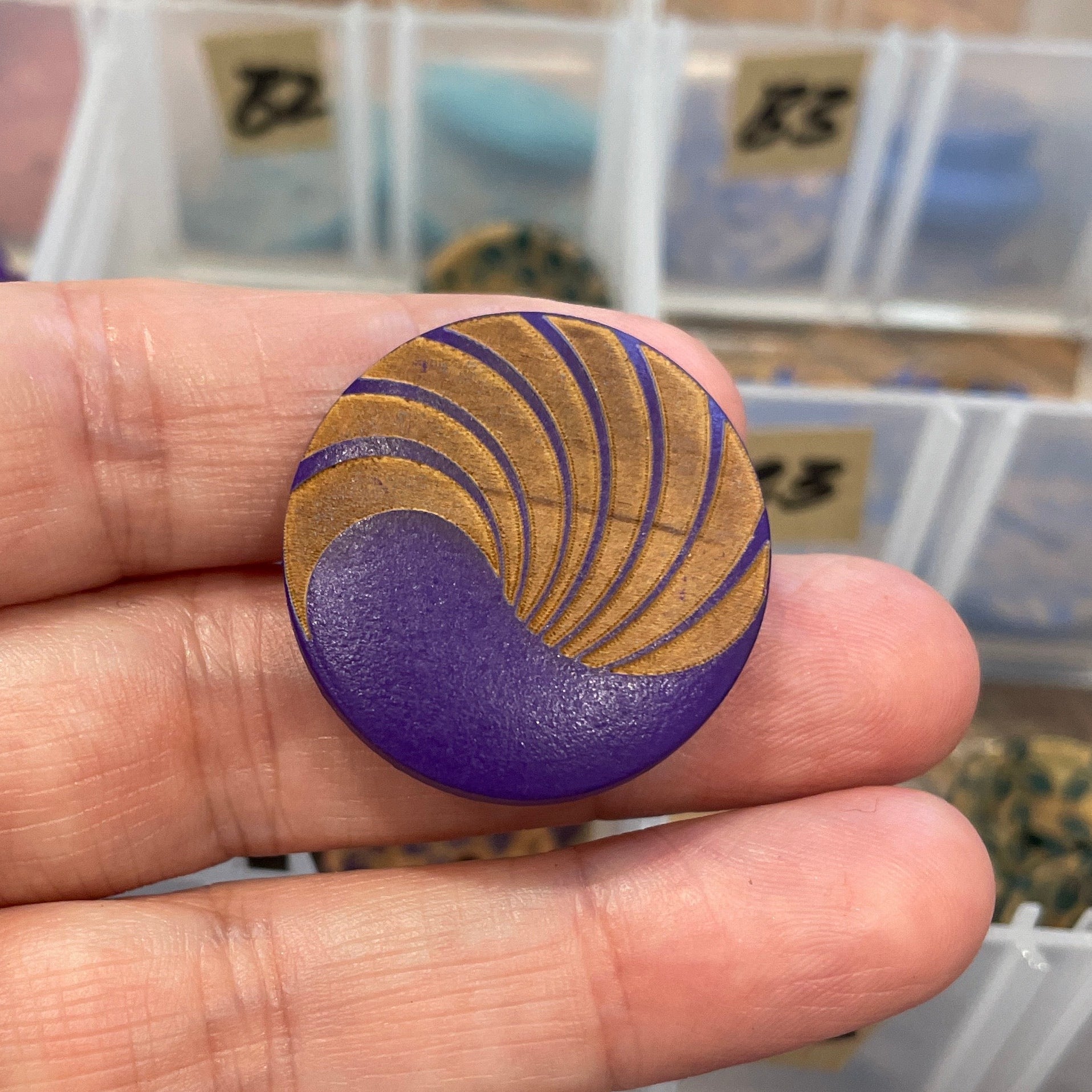 Hand holding a purple button with gold design in front of a clear container with buttons.