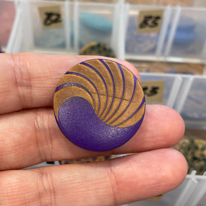 Hand holding a purple button with gold design in front of a clear container with buttons.