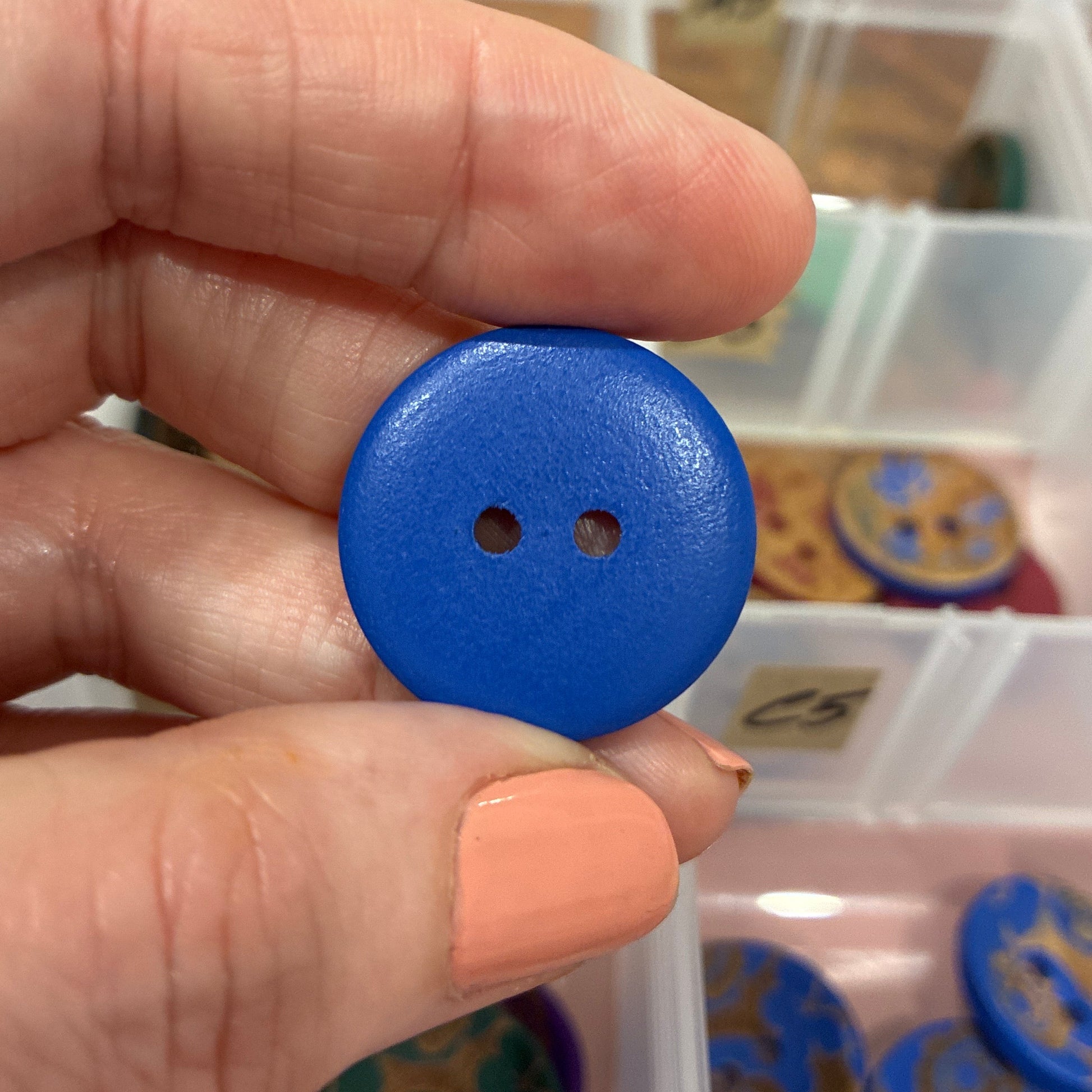 Blue button held between fingers with a container of buttons in the background