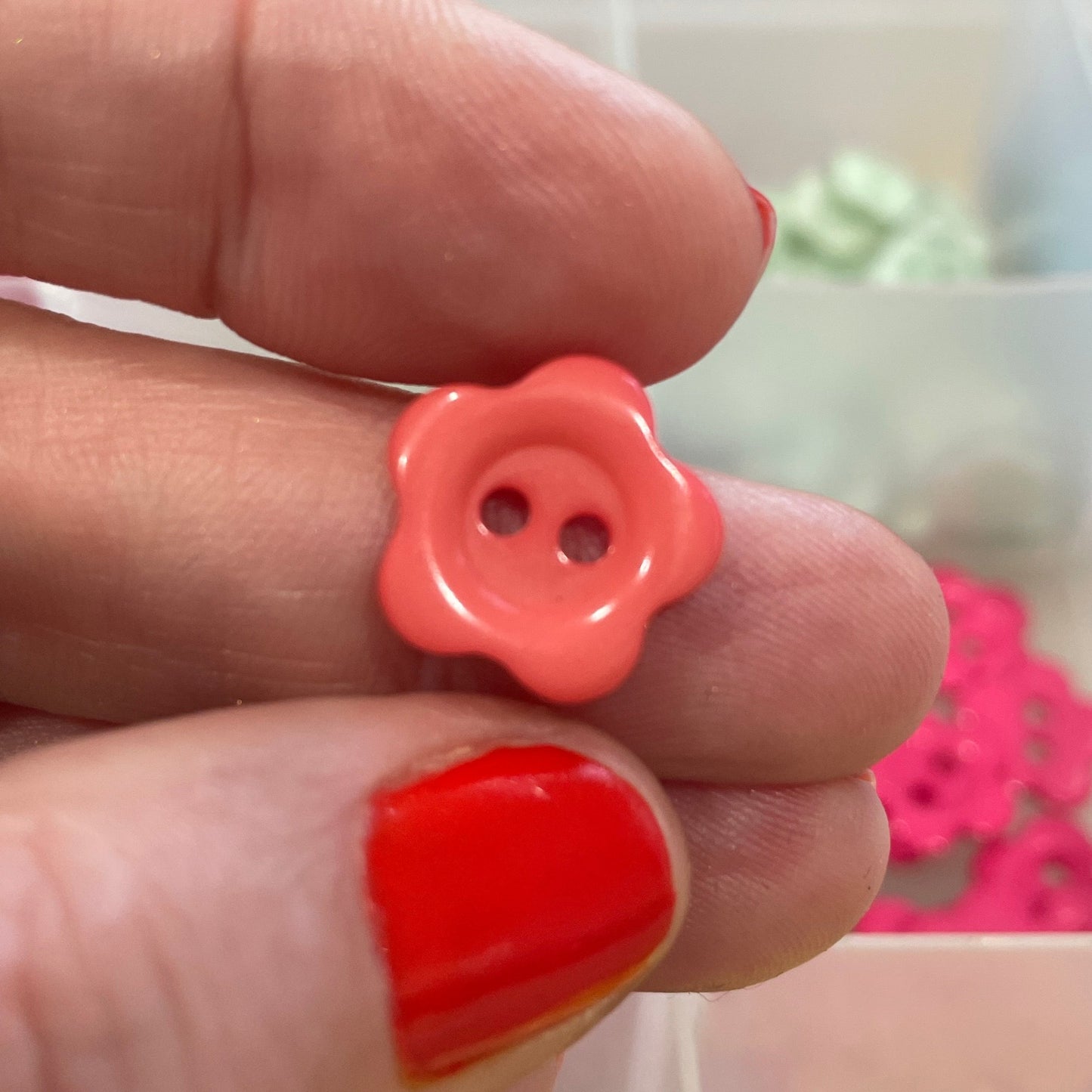 Hand holding a pink button with a blurred background of colorful buttons