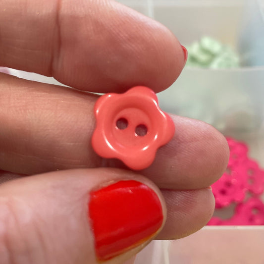 Hand holding a pink button with a blurred background of colorful buttons