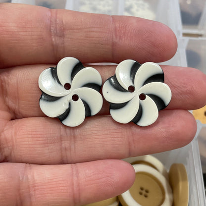 Black and white button with a star design held in a hand, with a container of buttons in the background.