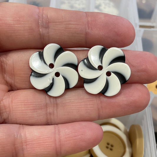 Black and white button with a star design held in a hand, with a container of buttons in the background.