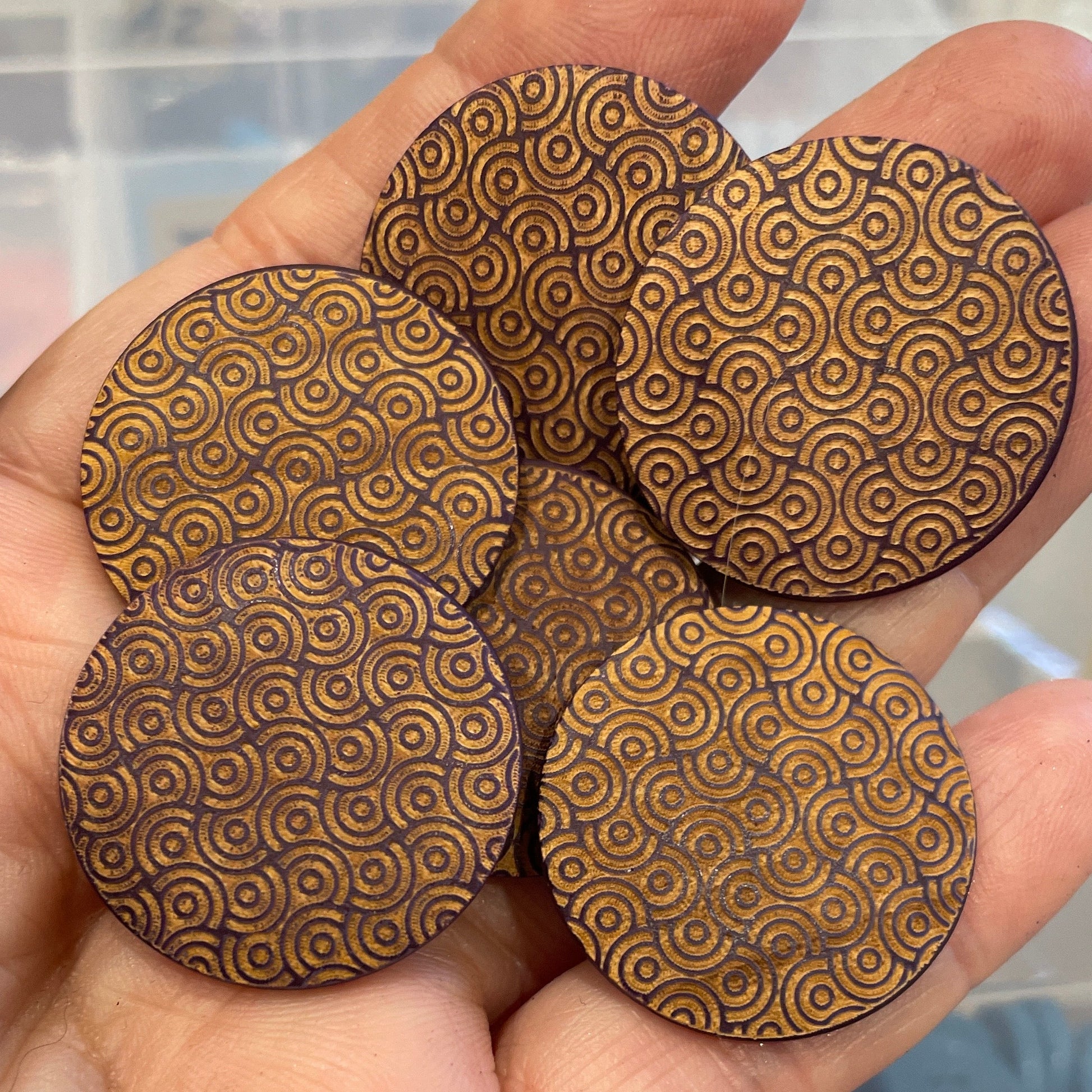 Hand holding four wooden circular buttons with a pattern, blurred background