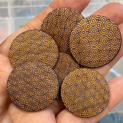 Hand holding four wooden circular buttons with a pattern, blurred background