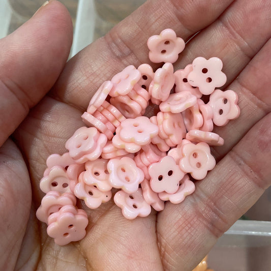Hand holding pink flower-shaped beads with a container of similar beads in the background.