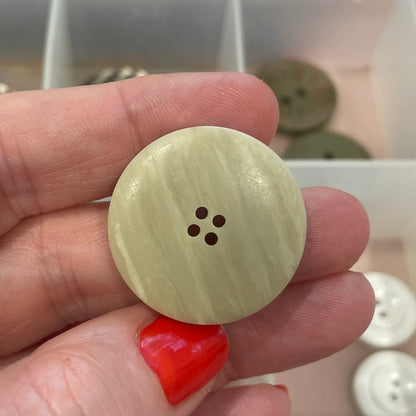 Hand holding a beige button with a clear container of buttons in the background