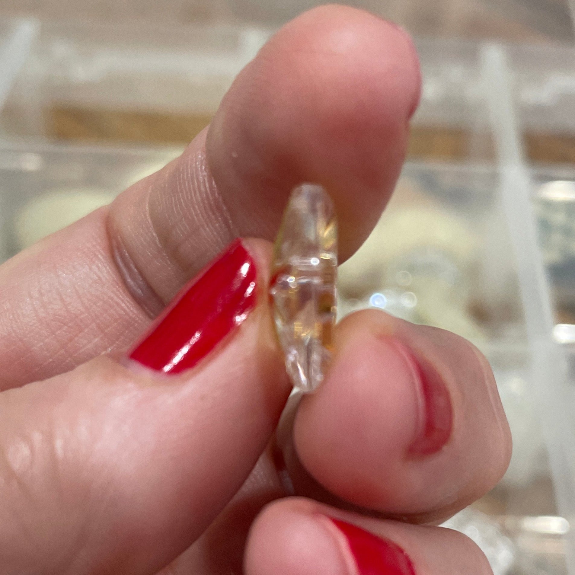 Hand holding a small clear object with red nail polish against a blurred background