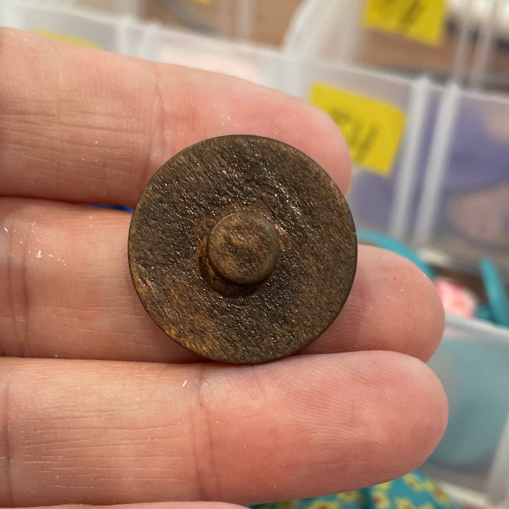 Hand holding a small metal object with a container of buttons in the background