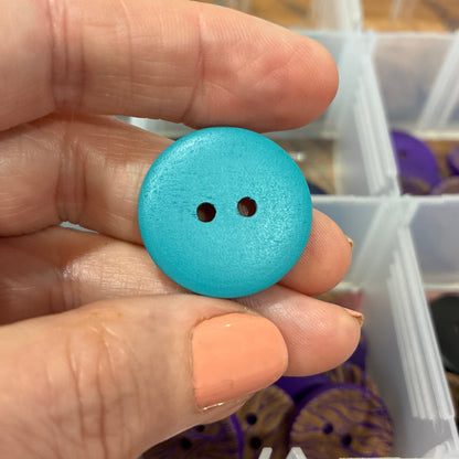 Hand holding a blue button with a background of various buttons in containers.