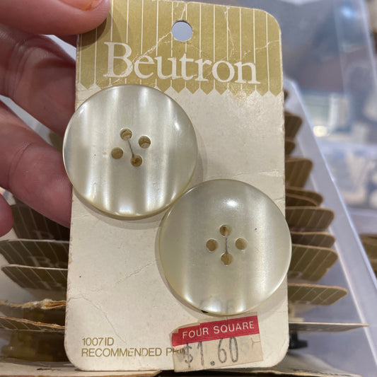 Two pearl buttons on a Boutton brand card held by a hand.