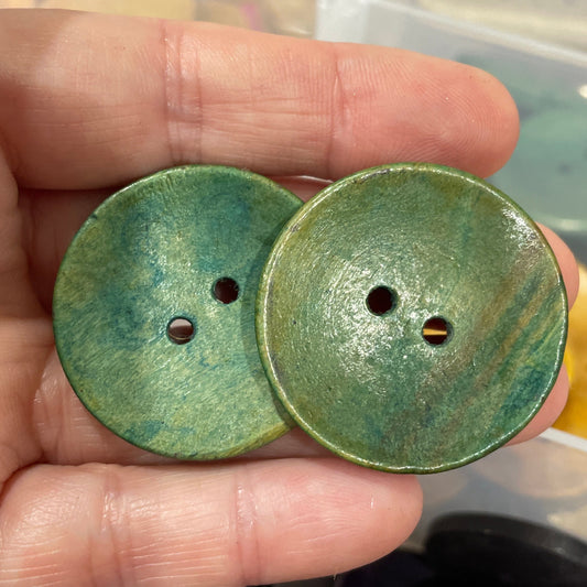 Green buttons held in a hand with a blurred background of more buttons.