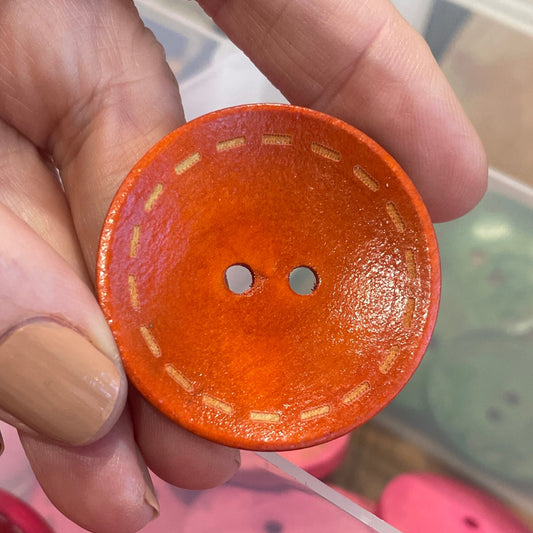Hand holding an orange button with a container of pink buttons in the background
