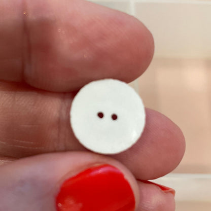 White button held between fingers with a background of various buttons