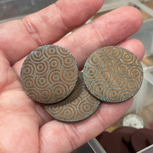 Hand holding two decorative buttons with a background of a button organizer.