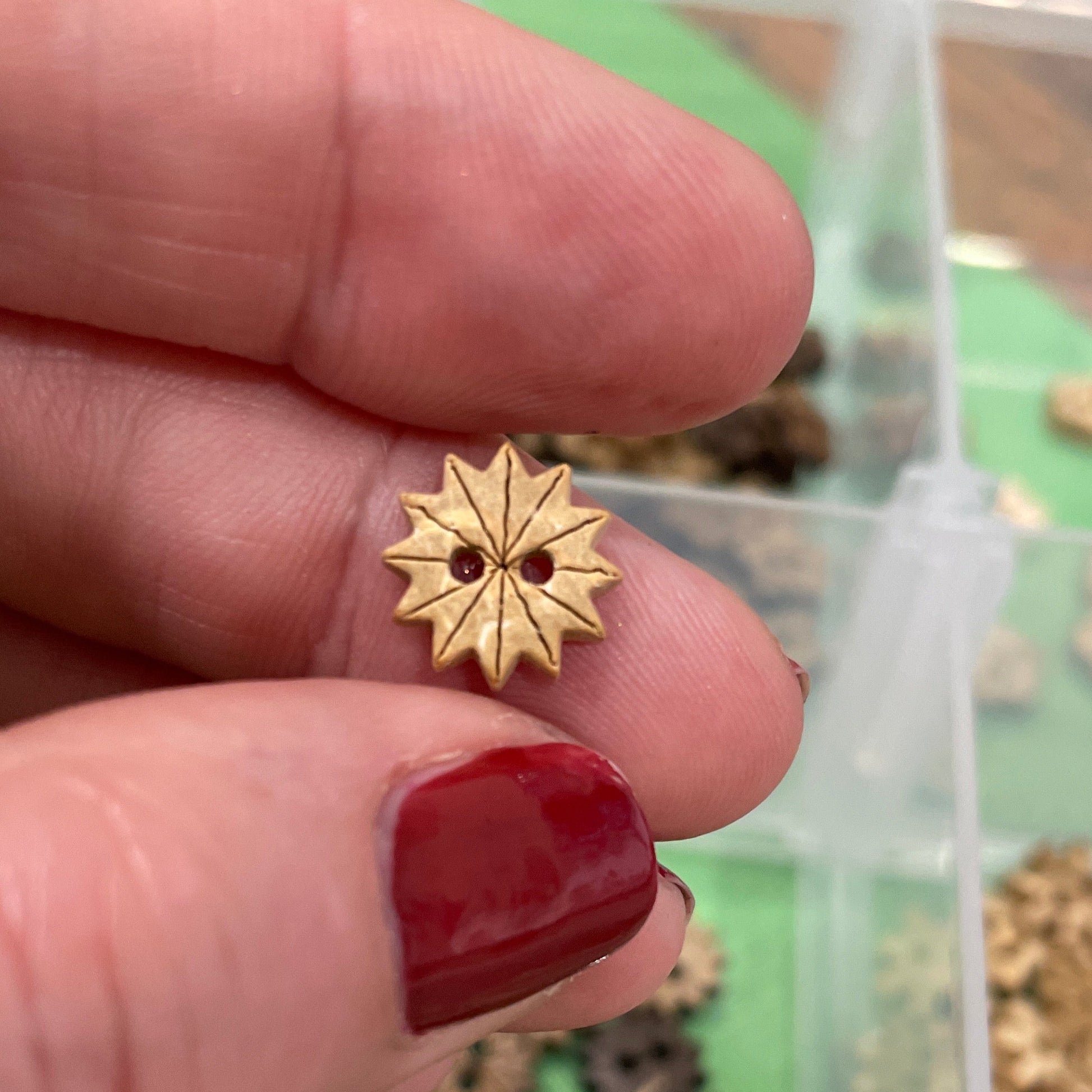 Gold star-shaped button  held between fingers with a container of similar buttons  in the background.
