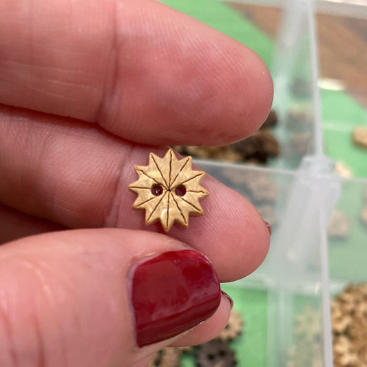 Gold star-shaped button  held between fingers with a container of similar buttons  in the background.