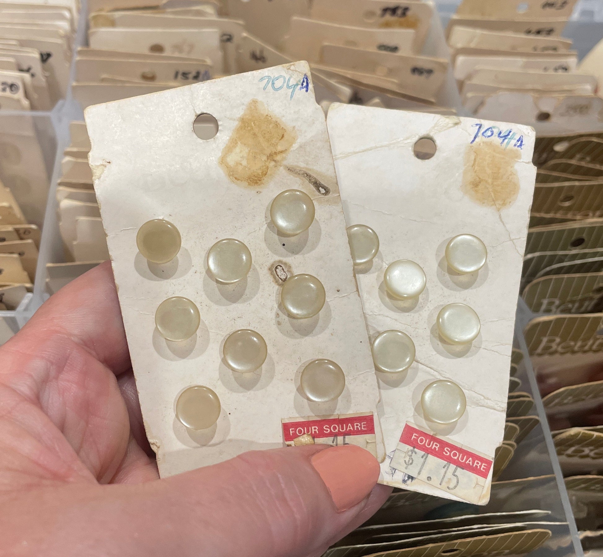 Hand holding a card with vintage buttons in front of a storage box filled with more buttons.