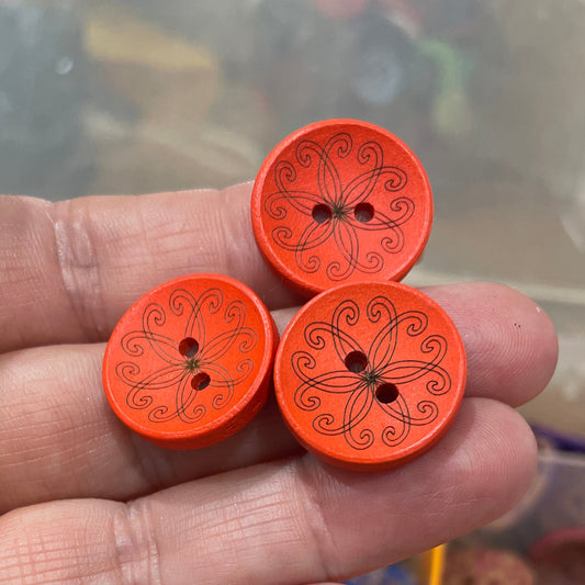 Hand holding three orange buttons with patterns, with a container of buttons in the background.