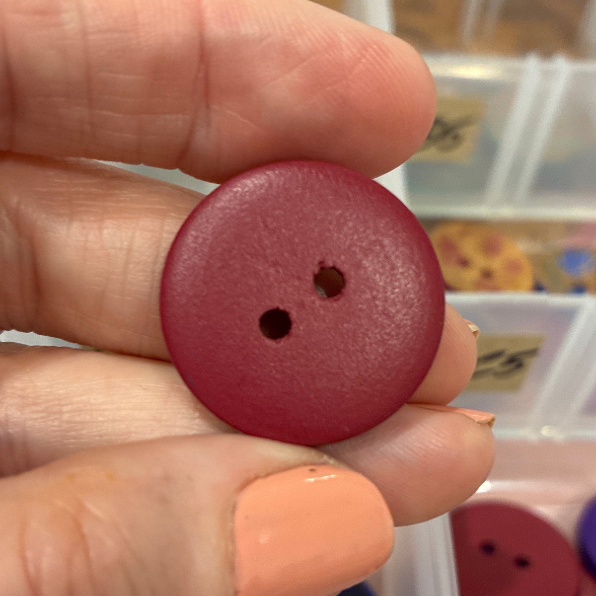 Maroon button held by a hand with a container of buttons in the background