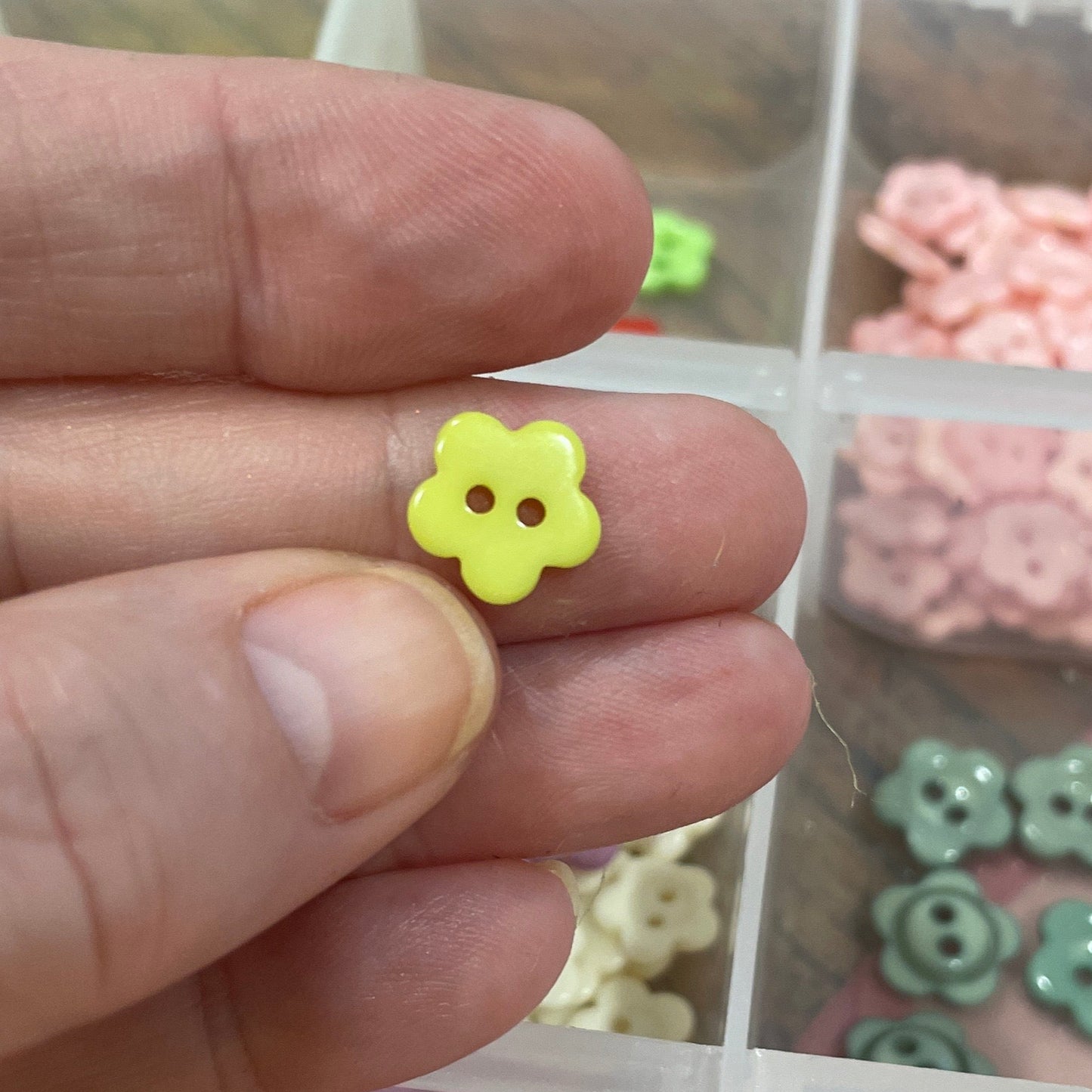 Hand holding a yellow flower-shaped object with a container of colorful flower-shaped objects in the background.
