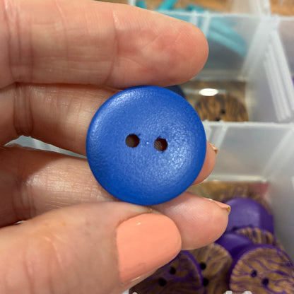 Hand holding a blue button with a blurred background of a storage box with buttons.