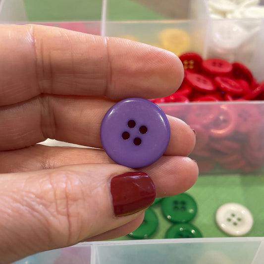 Hand holding a purple button with button collection in the background