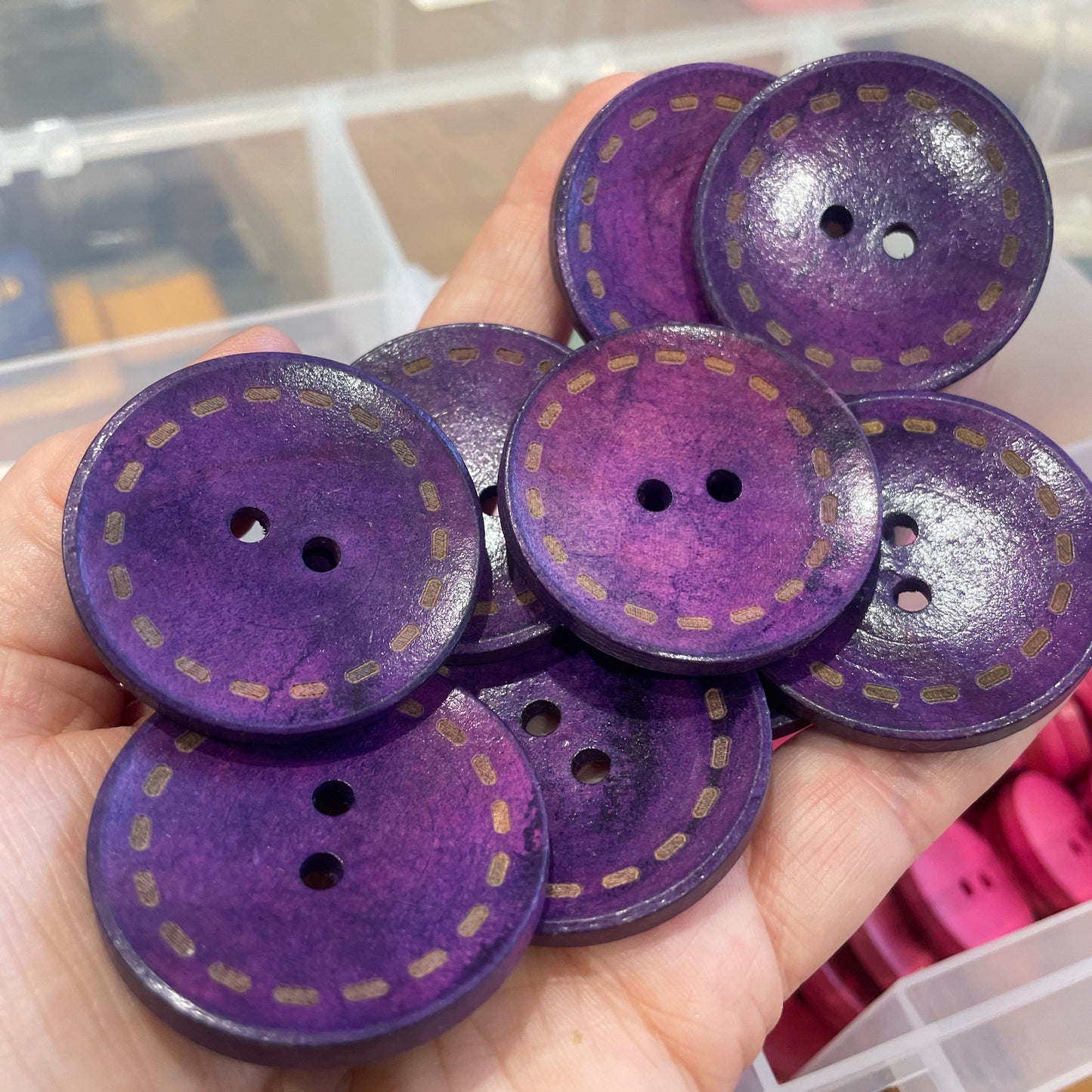Purple buttons with gold stitching held in a hand against a blurred background
