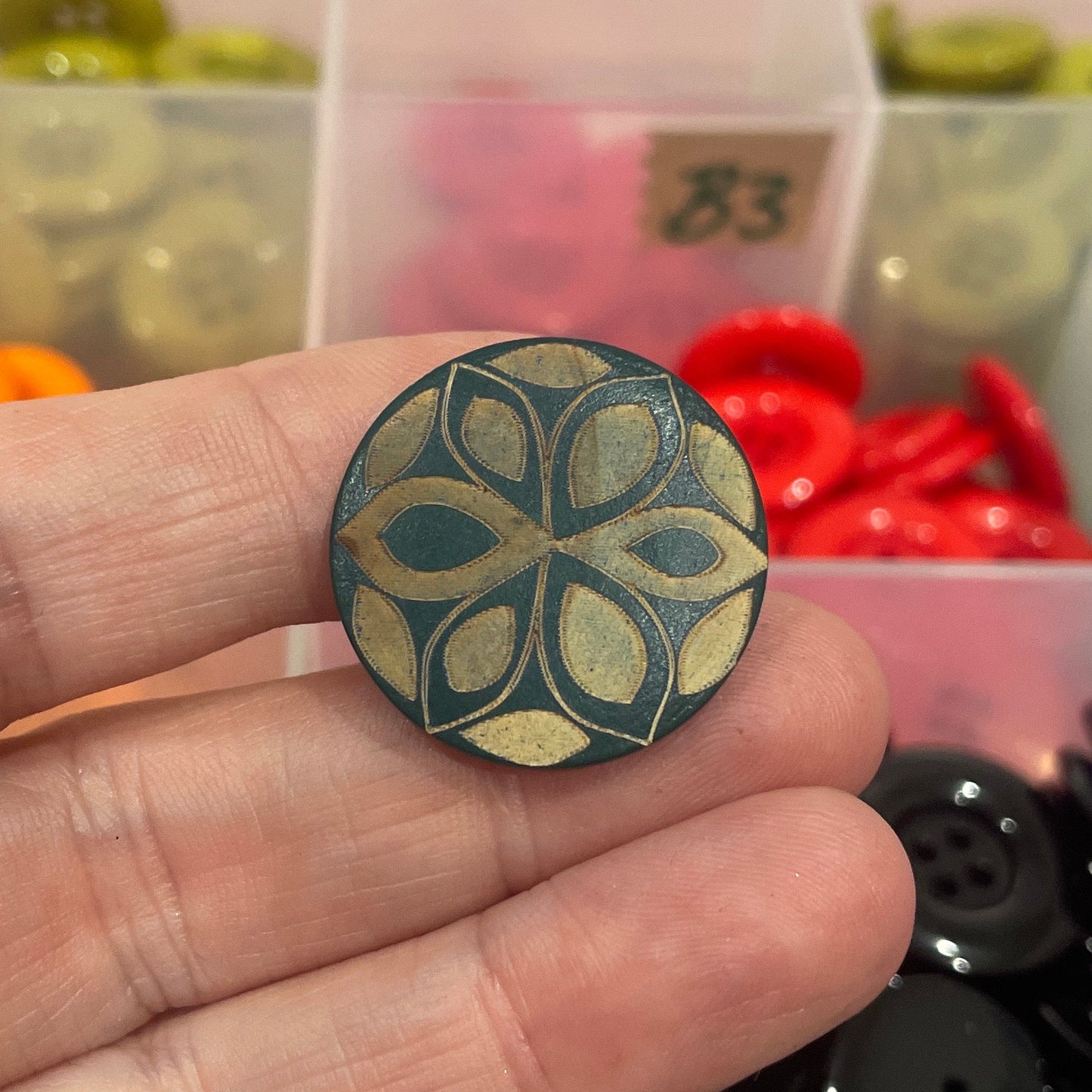Hand holding a decorative button with a colorful assortment of buttons in the background.