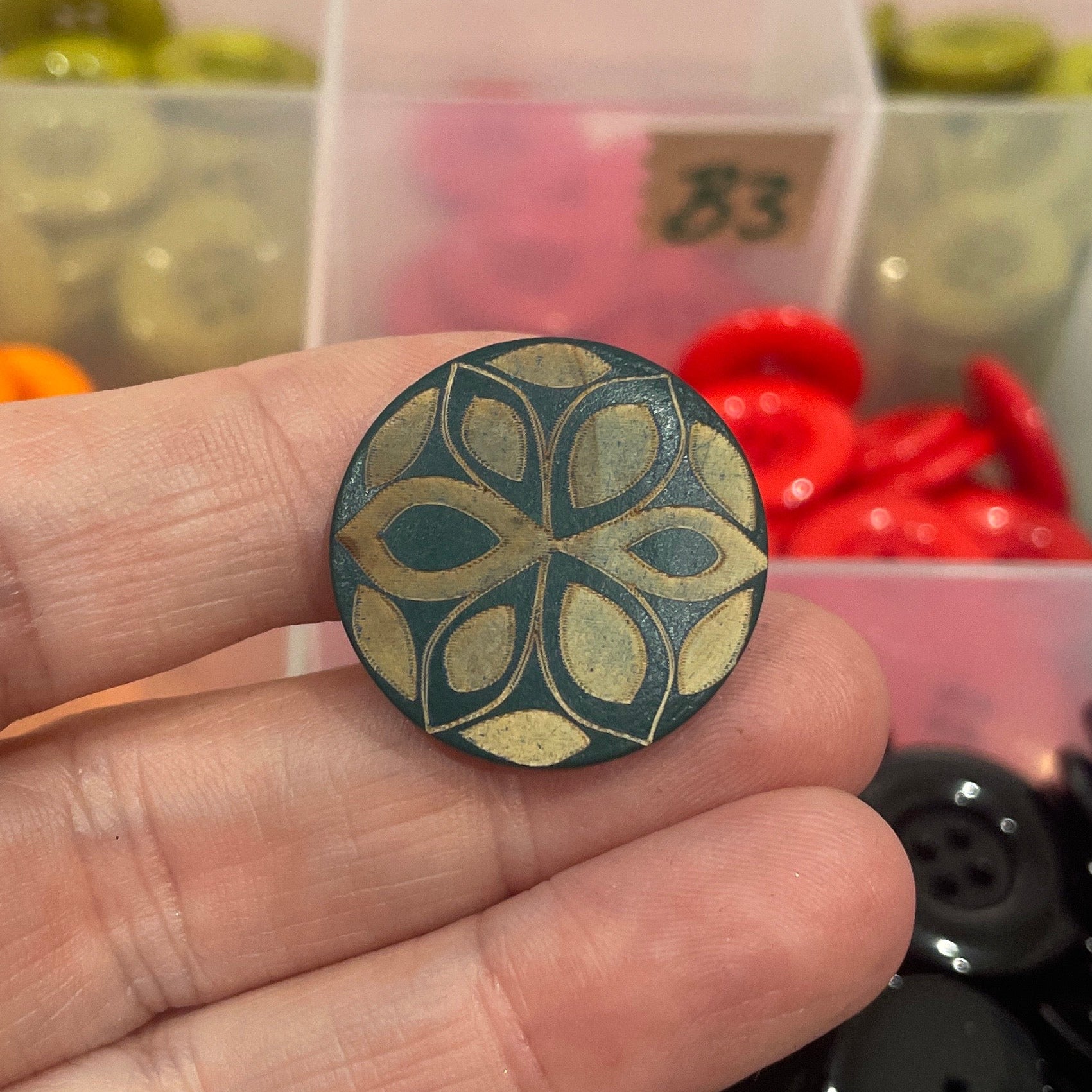 Hand holding a decorative button with a colorful assortment of buttons in the background.