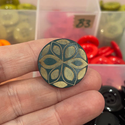 Hand holding a decorative button with a colorful assortment of buttons in the background.