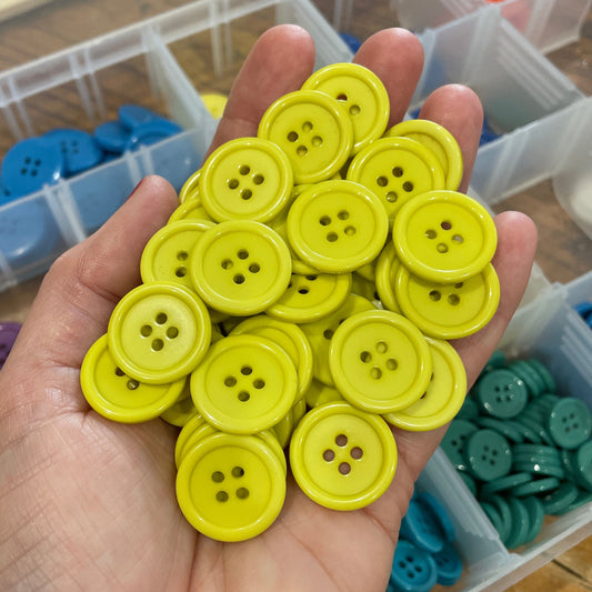 Hand holding a collection of yellow buttons with a container of buttons in the background.