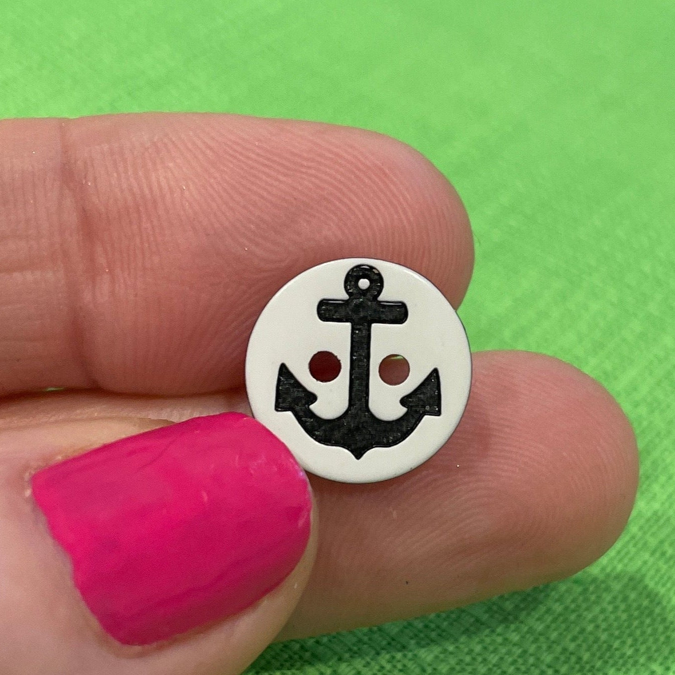 Small round object with a design held between fingers against a green background