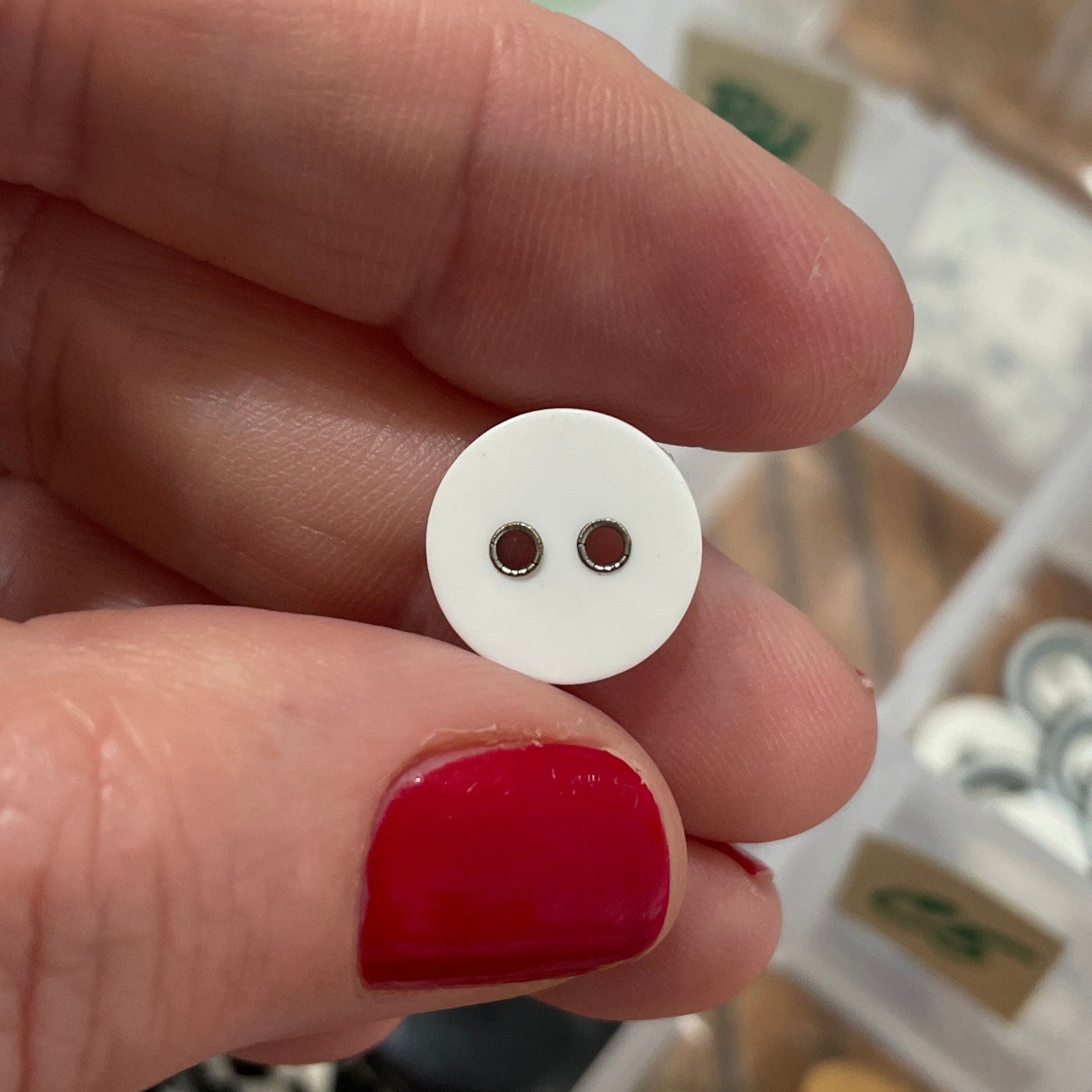 Hand holding a white button with two holes against a background of various buttons.