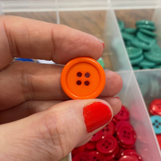 Hand holding an orange button with a container of colorful buttons in the background