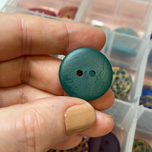 Hand holding a green button with a container of buttons in the background