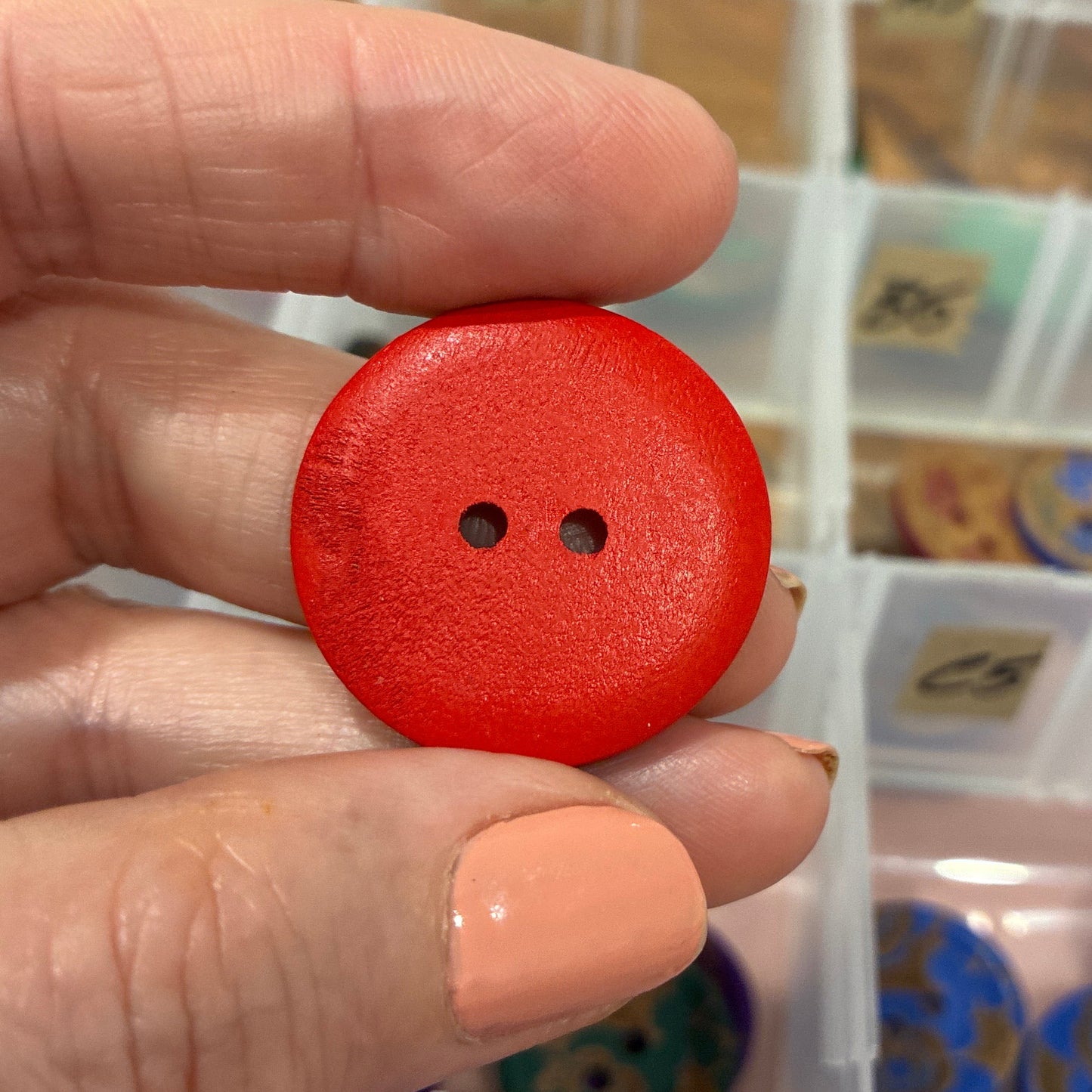 Hand holding a red button with a blurred background of a button organizer.
