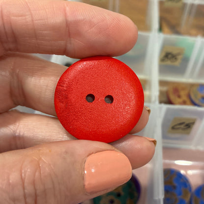 Hand holding a red button with a blurred background of a button organizer.