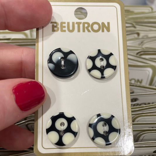 Set of black and white buttons on a BEUTRON card held by a person with red nail polish.