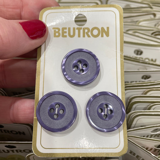 Blue buttons on a Beutron branded card held by a hand with red nail polish.