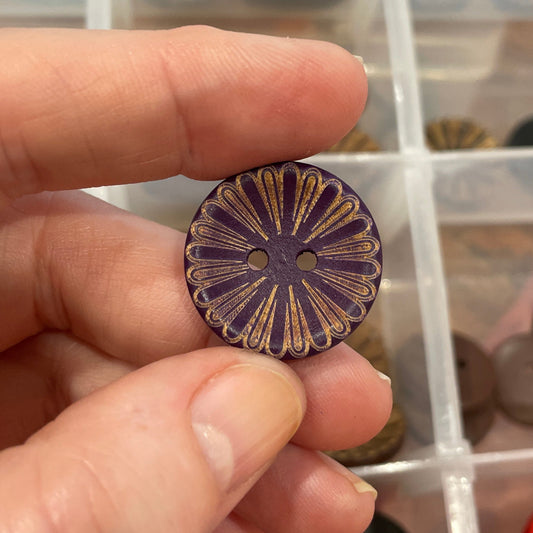 Hand holding a decorative button with a button collection box in the background