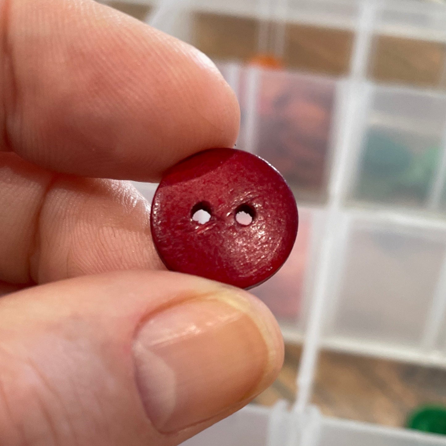 Red button held by a hand with a container of assorted buttons in the background
