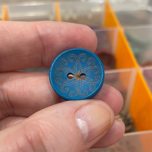 Hand holding a blue decorative button with a blurred background of button storage.