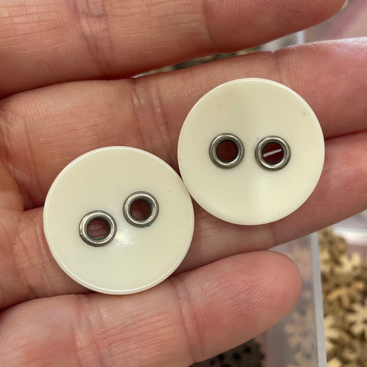 Two white buttons held in a hand with a container of buttons in the background.