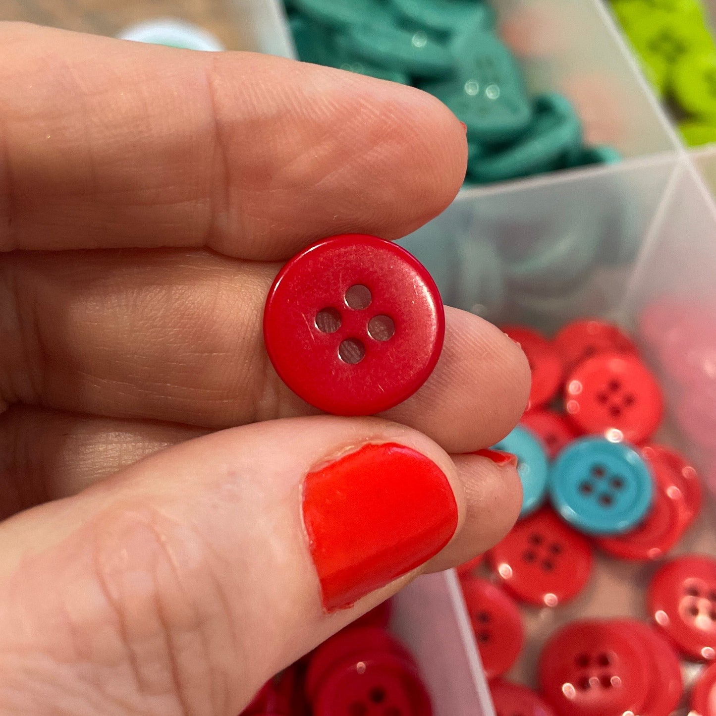 Hand holding a red button with a container of buttons in the background