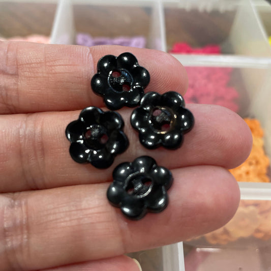Black flower-shaped beads on a hand with a blurred background of colorful items.