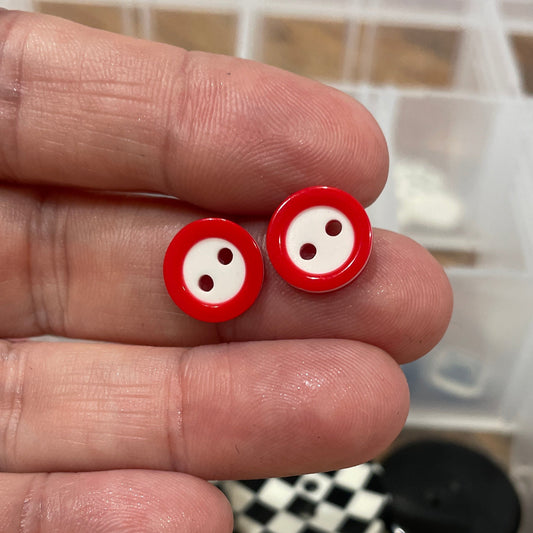 Red buttons held between fingers with a container of various buttons in the background